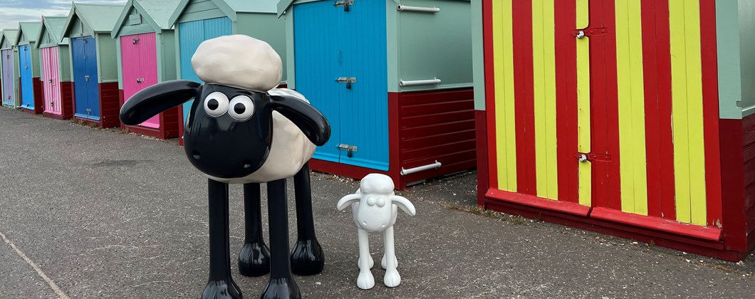 Large Shaun the Sheep next to a small uncoloured Shaun the sheep in front of beach huts
